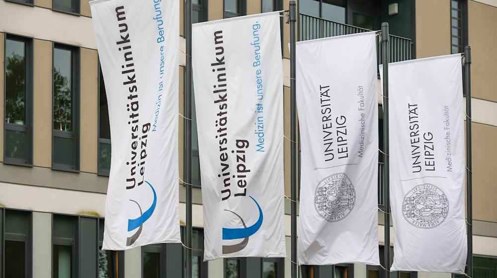 Banderas de la Universidad de Leipzig y del Hospital Universitario cuelgan delante de un edificio de la clínica / Foto: Jan Woitas/dpa