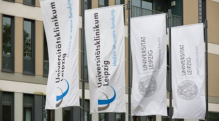 Flaggen der Universität Leipzig und des Universitätsklinikums hängen vor einem Gebäude der Klinik. / Foto: Jan Woitas/dpa