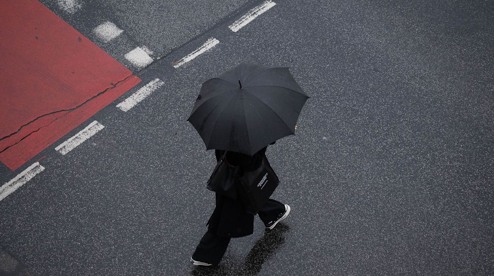 Mit einem Schirm schützt sich eine Passantin vor dem Regen. / Foto: Boris Roessler/dpa