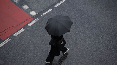 Mit einem Schirm schützt sich eine Passantin vor dem Regen. / Foto: Boris Roessler/dpa