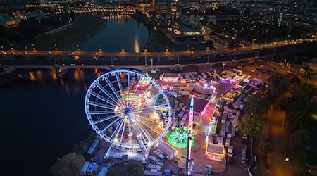 A Ferris wheel and rides are illuminated with colorful lamps in the evening at the autumn festival on the Pieschner Allee fairground / Photo: Robert Michael/dpa/Archivbild