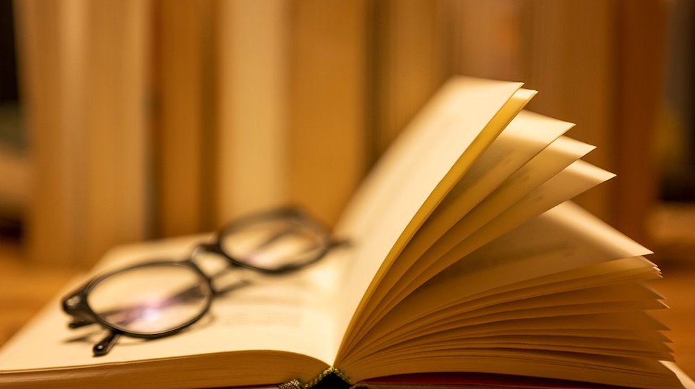 A pair of reading glasses lies on an open paper book / Photo: Monika Skolimowska/dpa/Illustration