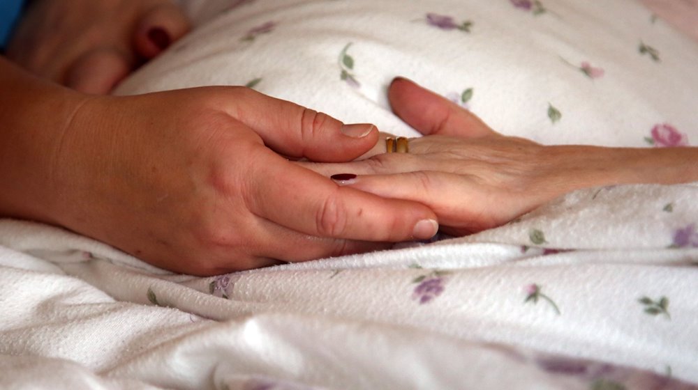 Hände auf der Bettdecke einer Bewohnerin in einem Hospiz. / Foto: Peter Förster/dpa-Zentralbild/dpa/Archivbild