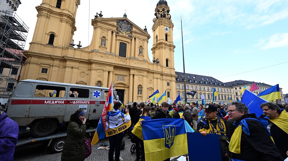 Protesters stand with Ukrainian flags in front of a shot-up ambulance at a demonstration during the security conference on Odeonsplatz. More than 160,000 war refugees from Ukraine are currently living in Bavaria / Photo: Felix Hörhager/dpa