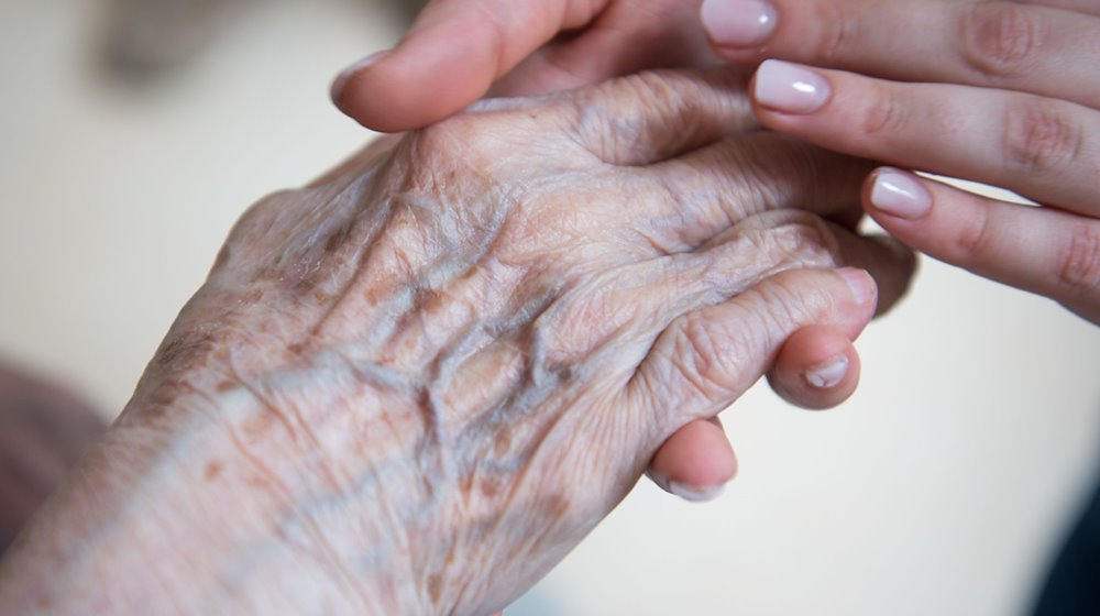 Eine Pflegerin hält die Hand einer Bewohnerin im Seniorenzentrum Sankt Elisabeth. / Foto: Christophe Gateau/dpa