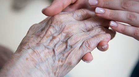 Eine Pflegerin hält die Hand einer Bewohnerin im Seniorenzentrum Sankt Elisabeth. / Foto: Christophe Gateau/dpa