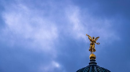 Dunkle Wolken ziehen über der goldenen Fama-Skulptur auf der Kuppel der Hochschule für Bildende Künste (HfBK). / Foto: Jens Büttner/dpa-Zentralbild/dpa/Archivbild