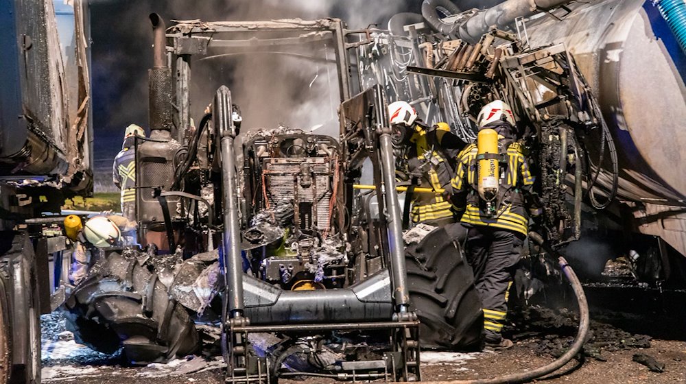 Feuerwehrleute stehen zwischen verbrannten landwirtschaftlichen Geräten. / Foto: Andre März/ErzgebirgsNews/dpa