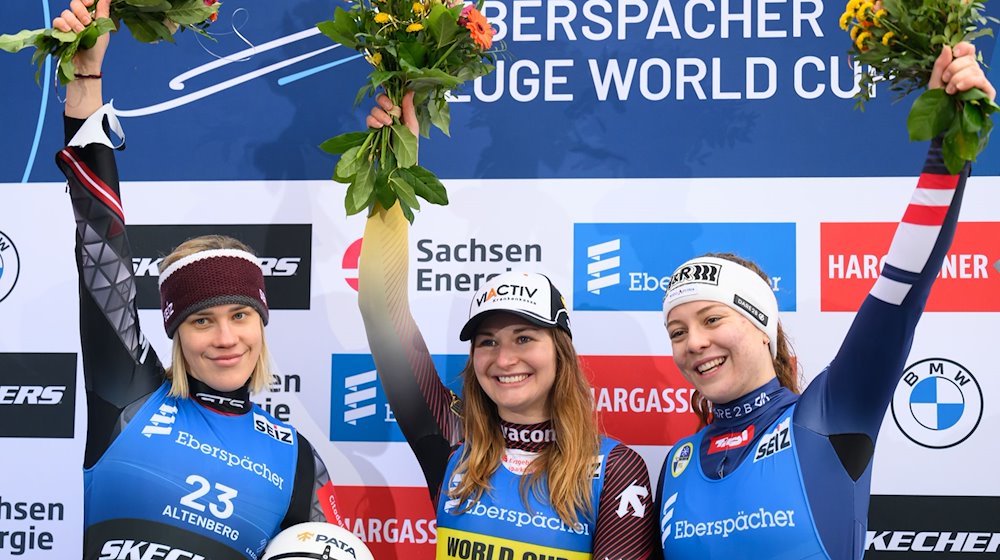 Winner Julia Taubitz (M) from Germany celebrates on the podium alongside runner-up Elina Iva Viola (l) from Latvia and third-placed Lisa Schulte from Austria / Photo: Robert Michael/dpa