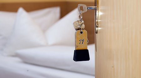 Una llave de habitación cuelga de la cerradura de la puerta frente a una cama en una casa de huéspedes / Foto: Swen Pförtner/dpa