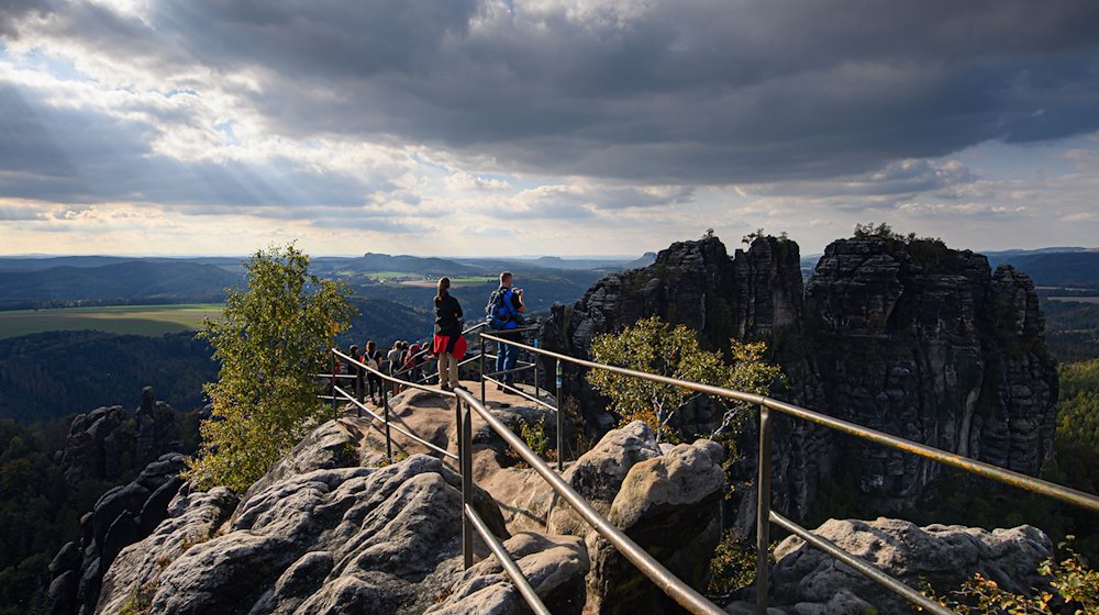 Wanderer blicken von der Schrammsteinaussicht in der Sächsischen Schweiz auf die Felsen der Schrammsteine. / Foto: Robert Michael/dpa-Zentralbild/dpa