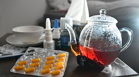 Medication and a pot and cup of tea to fight the flu are placed on a bedside table. / Photo: Bernd Weißbrod/dpa