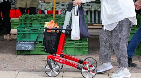 Eine Seniorin geht mit ihrem Rollator über den Wochenmarkt in der Innenstadt. / Foto: Jan Woitas/dpa