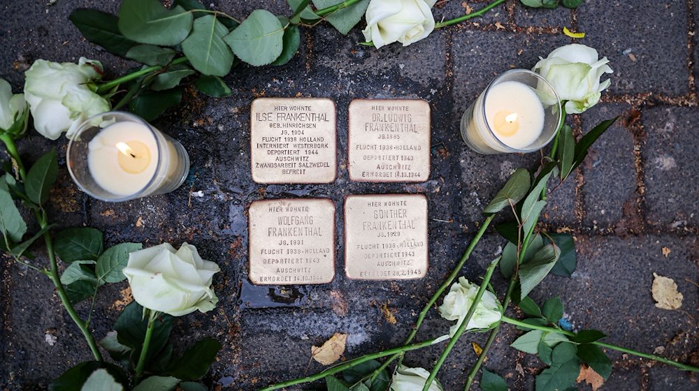 Weiße Rosen und Kerzen liegen und stehen neben den Stolpersteinen, die an das Schicksal der jüdischen Familie Frankenthal erinnern. / Foto: Jan Woitas/dpa