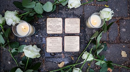 Weiße Rosen und Kerzen liegen und stehen neben den Stolpersteinen, die an das Schicksal der jüdischen Familie Frankenthal erinnern. / Foto: Jan Woitas/dpa