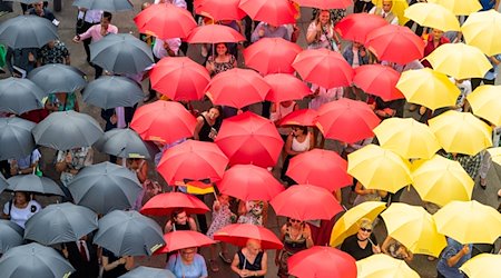 Eingebürgerte Menschen stehen mit schwarz-rot-goldenen Regenschirmen nach dem Einbürgerungsfest vor dem Sächsischen Landtag. / Foto: Robert Michael/dpa-Zentralbild/dpa/Archivbild