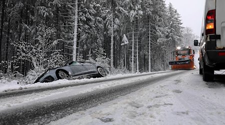 Ein Auto steht nach einem Unfall neben der schneebedeckten Fahrbahn im Graben, während ein Räumfahrzeug angefahren kommt. / Foto: News5 / März/NEWS5/dpa