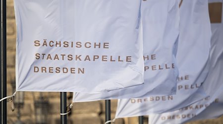 Flags with the inscription "Sächsische Staatskapelle Dresden" wave in the wind in front of the Semperoper / Photo: Robert Michael/dpa