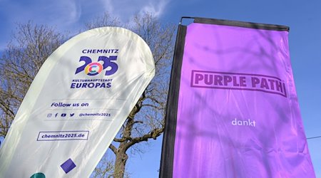 يرفع اثنان من الأعلام بجانب بعضهما «كيمنيتس 2025، عاصمة ثقافة أوروبية» و «Purple Path». / صورة: هايكو ريبش / دبي