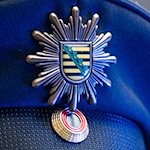 Das Wappen der sächsischen Polizei ist an der Mütze eines Polizisten angebracht. / Foto: Robert Michael/dpa/Symbolbild