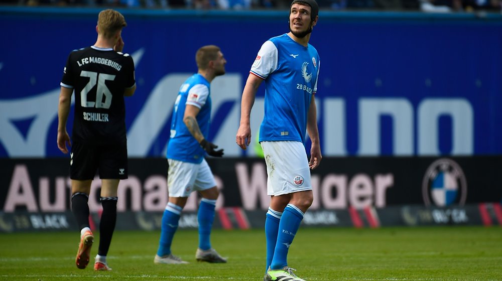 Rostock's Damian Roßbach (r) looks at the scoreboard during a stoppage in play. / Photo: Gregor Fischer/dpa