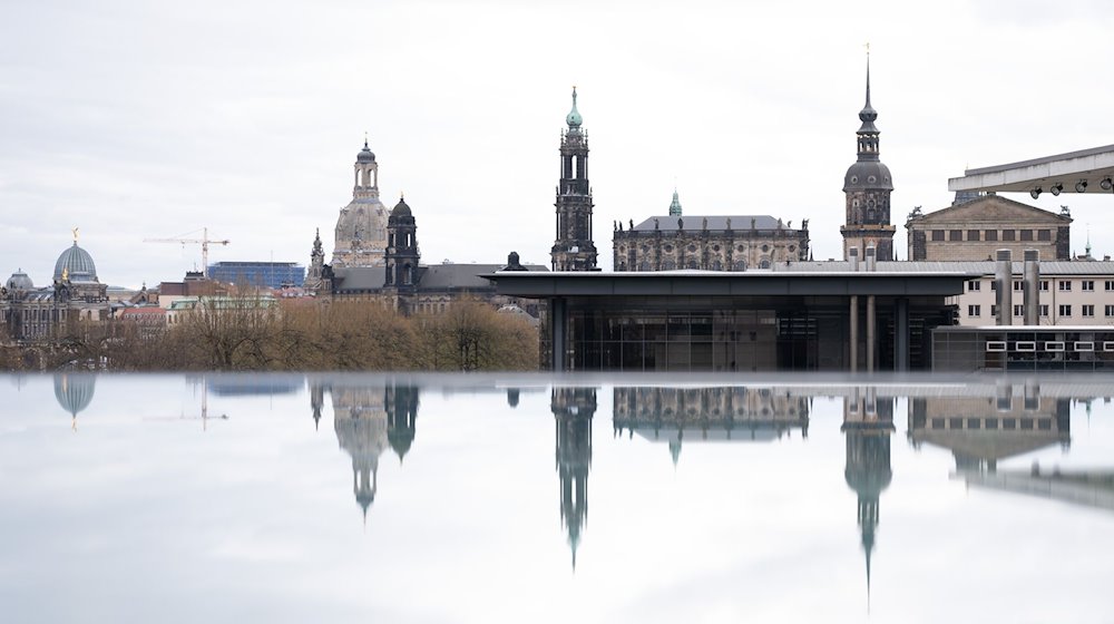 Die Kulisse der Dresdner Altstadt mit der Frauenkirche (l-r), dem Ständehaus, der katholischen Hofkirche, dem Schlossturm und der Semperoper spiegelt sich in einer mit Regenwasser bedeckten Scheibe. / Foto: Sebastian Kahnert/dpa