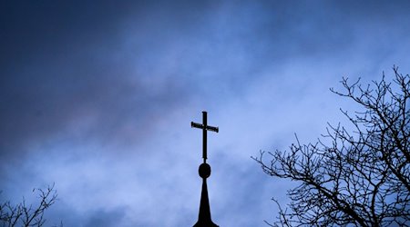 Dunkle Wolken ziehen über das Kreuz auf einer Kirche hinweg. / Foto: Julian Stratenschulte/dpa/Symbolbild