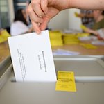 Ein Stimmzettelumschlag für die Briefwahl wird in eine Wahlurne geworfen. / Foto: Robert Michael/dpa/Symbolbild
