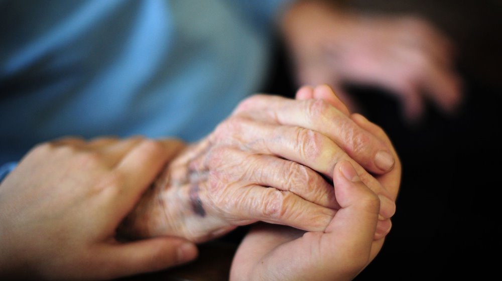 Eine Pflegekraft hält in einem Seniorenheim die Hand einer Bewohnerin. / Foto: Daniel Reinhardt/dpa/Archiv