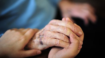 Eine Pflegekraft hält in einem Seniorenheim die Hand einer Bewohnerin. / Foto: Daniel Reinhardt/dpa/Archiv