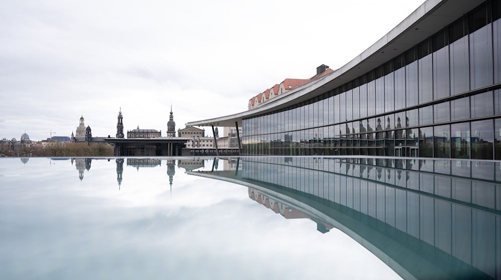 Die Kulisse der Dresdner Altstadt mit der Frauenkirche (l-r), dem Ständehaus, der katholischen Hofkirche, dem Schlossturm und der Semperoper spiegelt sich am Kongresszentrum in einer mit Regenwasser bedeckten Scheibe. / Foto: Sebastian Kahnert/dpa