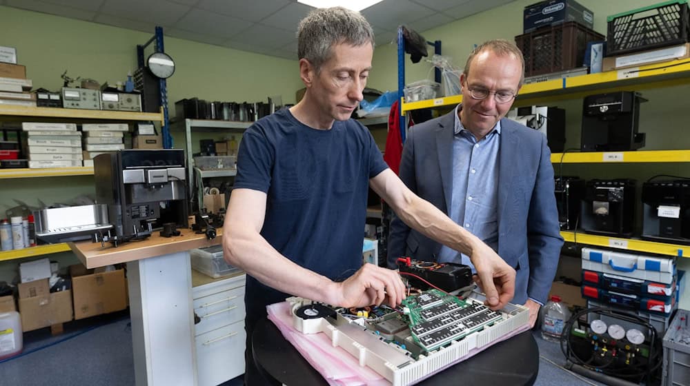 Wolfram Günther (Bündnis90/Die Grünen), Umweltminister von Sachsen, beobachtet Lothar Prohl, Servicetechniker, in der Werkstatt der HSC HomeElectronic Service Center GmbH in Leipzig bei der Reparatur eines Ceranfelds. / Foto: Hendrik Schmidt/dpa/Archivbild