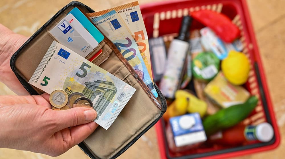 Una mujer sostiene dinero en la mano delante de una cesta llena de comestibles. / Foto: Patrick Pleul/dpa