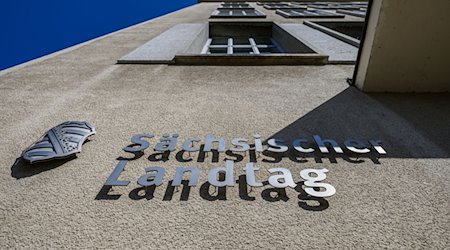 Sächsischer Landtag und eine Wappen von Sachsen sind an der Fassade des Parlamentsgebäudes montiert. / Foto: Robert Michael/dpa