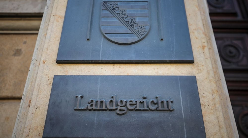 Ein Schild und das sächsische Wappen hängen am Eingang zum Landgericht Leipzig. / Foto: Jan Woitas/dpa/Archivbild