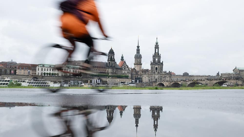 Ein Radfahrer fährt am Ufer entlang. Die Kulisse der Altstadt spiegelt sich in einer Pfütze am Ufer der Elbe. / Foto: Sebastian Kahnert/dpa