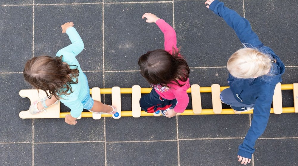 Kinder balancieren während eines Pressetermins auf dem Spielplatz einer Kindertagesstätte auf einem Brett. / Foto: Sebastian Kahnert/dpa