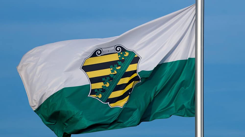 Die Flagge vom Bundesland Sachsen mit dem sächsischen Wappen weht im Wind. / Foto: Monika Skolimowska/zb/dpa/Symbolbild