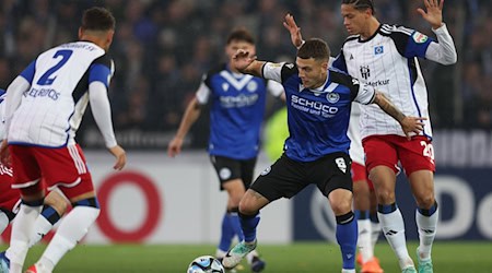 Soccer: DFB Cup, 2nd round, Arminia Bielefeld - Hamburger SV, in the Schüco-Arena. Bielefeld's Can Özkan (center) battling for the ball with Hamburg players William Mikelbrencis (left) and András Németh (right). The midfielder is moving to Aue / Photo: Friso Gentsch/dpa