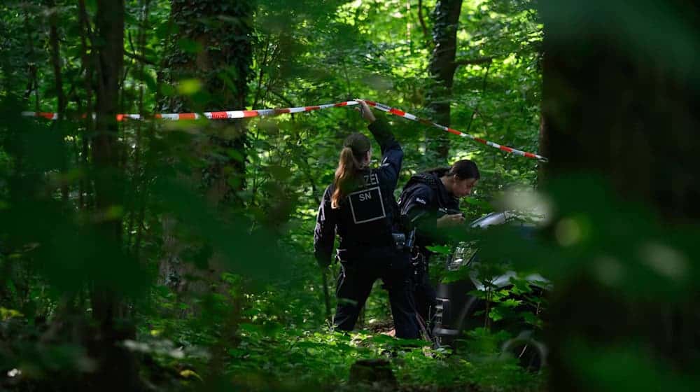 Eine Polizistin hält in einem Wald Absperrband hoch. / Foto: Robert Michael/dpa