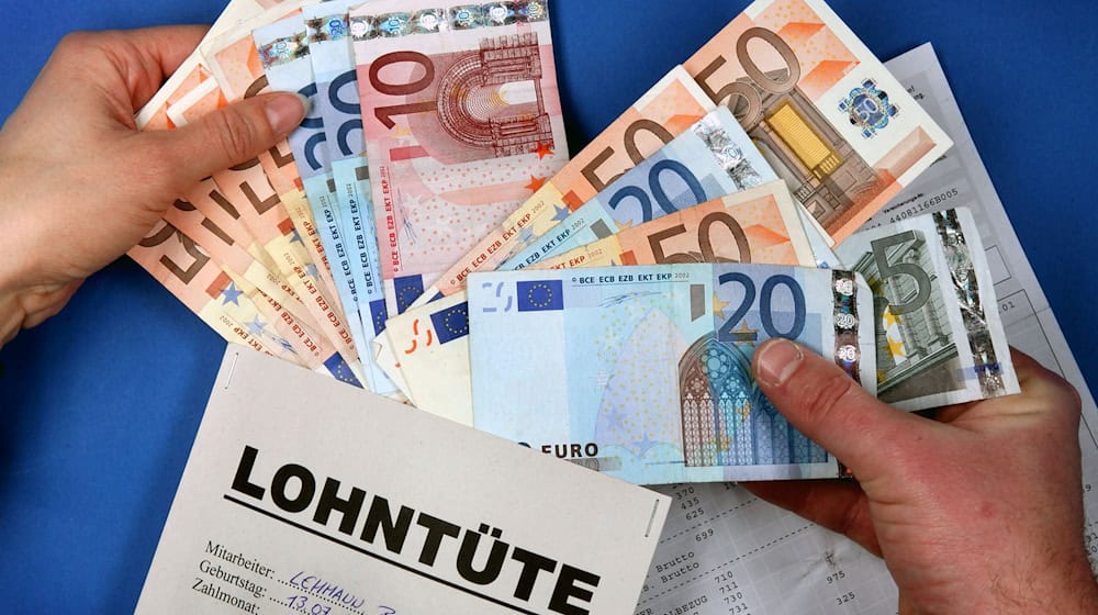 Zwei Hände stecken symbolisch in Schwerin Euro-Geldscheine in eine Lohntüte. / Foto: Jens Büttner/dpa-Zentralbild/dpa/Archivbild