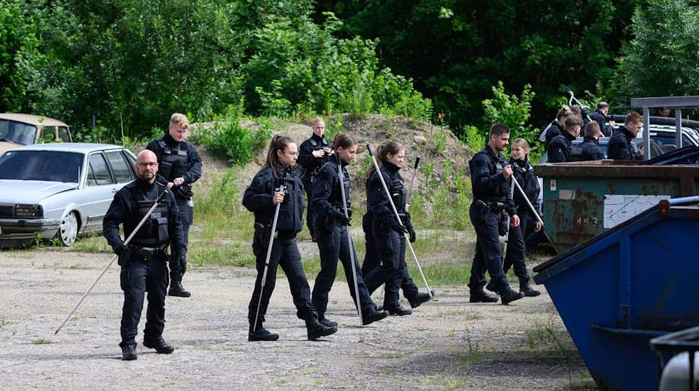 Polizisten sind mit Suchstangen auf der Suche nach einer vermissten Grundschülerin auf einem Firmengelände unterwegs. / Foto: Robert Michael/dpa