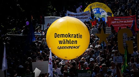 Teilnehmer halten einen gelben Ballon von Greepeace mit dem Text "Demokratie Wählen" bei einer Demonstration an der Siegessäule am Tag vor den Europawahlen gegen Rechtsextremismus und für eine demokratische, offene und vielfältige Gesellschaft. / Foto: Carsten Koall/dpa