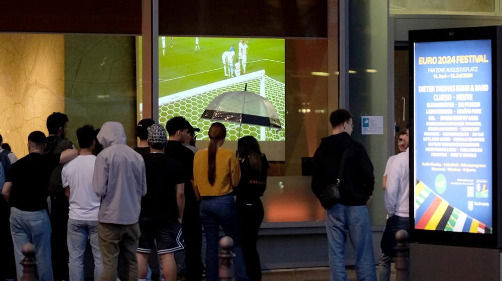 Fußballfans stehen vor dem Fenster eines Hotels und verfolgen das Spiel. / Foto: Sebastian Willnow/dpa/Archivbild