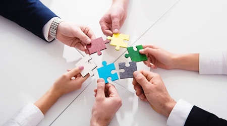 6 hands each hold a colorful puzzle piece together to form a circle.