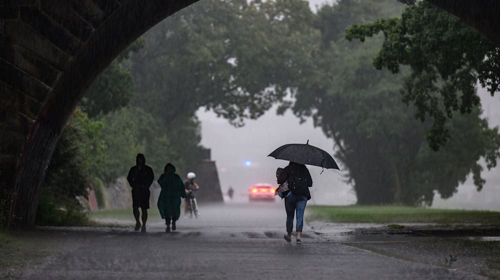 Menschen sind bei starkem Regen in Dresden während eines Gewitters auf dem Elberadweg unterwegs. / Foto: Robert Michael/dpa