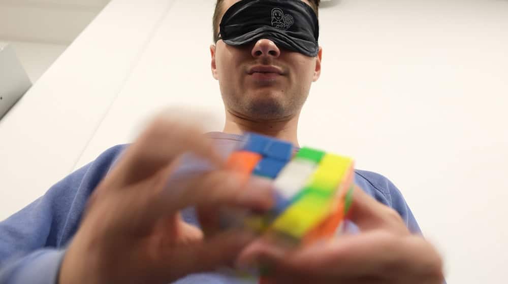 Un participante con los ojos vendados en el campeonato alemán del "Cubo de Rubik" se entrena para devolver el cubo a su forma original. / Foto: Sebastian Willnow/dpa