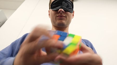 A blindfolded participant in the German "Rubik's Cube" championship trains to turn the cube back to its original shape. / Photo: Sebastian Willnow/dpa