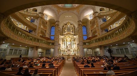 Gäste sitzen im Innenraum der Dresdner Frauenkirche unter der Sandsteinkuppel mit Blick auf den Altarraum (Archivbild). / Foto: Robert Michael/dpa-Zentralbild/dpa