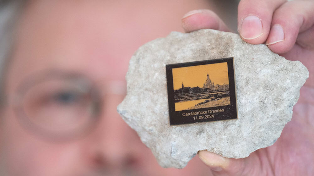 Torsten Daae, Geschäftsführer im Dresdner Laden «Catapult», hält einen Stein des abgerissenen Brückenteils der eingestürzten Carolabrücke mit einer Plakette in der Hand. / Foto: Sebastian Kahnert/dpa